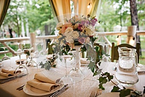 A big bouquet and a lot of cutlery are standing on the table. Restauraunt terrace on the background