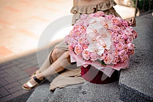 Big bouquet of pink roses and orchids in red round box stands on the steps.