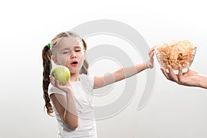 Big bowl of chips and fruit, beautiful little girl eats an apple, child is given a bowl of chips, white background and