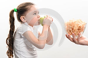Big bowl of chips and fruit, beautiful little girl eats an apple, child is given a bowl of chips, white background and