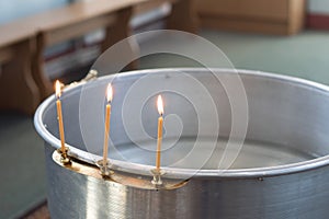 Big bowl of water for the baptism of a baby with wax candles. Orthodoxy. Greek Catholics