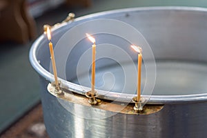 Big bowl of water for the baptism of a baby with wax candles. Orthodoxy. Greek Catholics. three candles burn to the side.