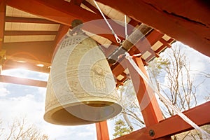 Big brass Buddhist bell and timber knock of Japanese temple in red pavilion on bright blue sky