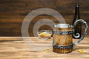 Big brown mug of beer,ale bottle and crispy snacks, pretzels, corn, nuts in bowl on wooden table, background close up