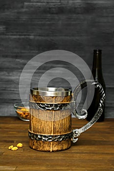 Big brown mug of beer,ale bottle and crispy snacks, pretzels, corn, nuts in bowl on wooden table, background close up