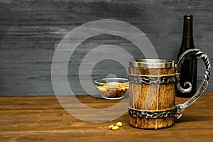 Big brown mug of beer,ale bottle and crispy snacks, pretzels, corn, nuts in bowl on wooden table, background close up. Alcohol