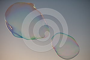 Big bubble flying over blue sky. Huge colorful soap bubbles fly over cloudy sky background.