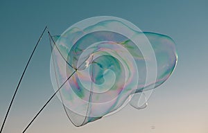 Big bubble flying over blue sky. Huge colorful soap bubbles fly over cloudy sky background.