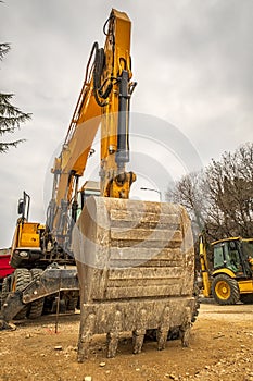 Big bucket and manipulator of excavator arm with hydraulic Hoses and cylinder in action.