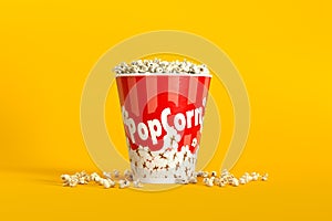 Big bucket of popcorn with spilled corns on yellow background