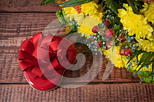 Big bunch with beautiful yellow chrysanthemums and rose hips with red gift box as heart with bow on wooden background, happy