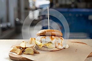 Big burger or cheeseburger serving with french fries on a wooden plate on cafe interior, selective focus