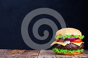 Big burger on wooden table with blank black chalkboard on background