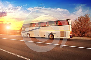 Big bus on the countryside road with trees and bushes against sky with sunset