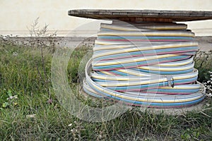 Big cable drum with colored wire lying on green grass