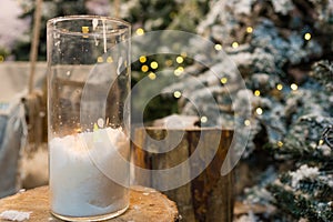 Big candles in glass vases in a snow-covered park or a forest while snowing