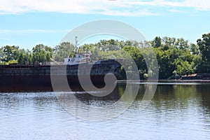 Big cargo ship are near shore with trees on river at summe