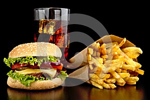 Big cheeseburger with glass of cola and french fries on black de