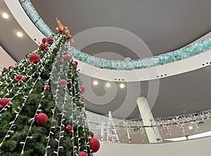a big christmas tree inside a shopping mall seen from below in perspective, decorated with red balls and a big star at the top,