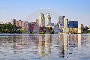 Big city on the banks wide river. Beautiful modern towers, buildings, skyscrapers are reflected in the water on summer morning.