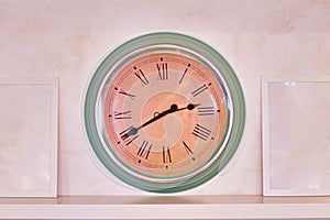 Big clock on the shelf. Blank photo frames on the wall. Green and beige color of the clock antique
