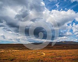 Big cloud over the autumn valley. Dramatic cloudscape. Sunny light through dark heavy thunderstorm clouds before rain. Overcast