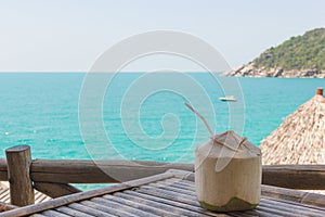 Big coconut with straw on bamboo table overlooking the sea