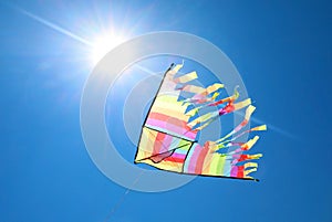 big colorful kite flying in the blue backlit sky and the glow of photo