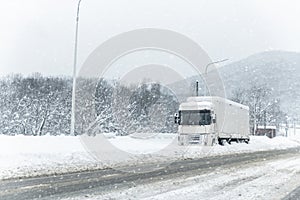 Big commercial semi-trailer truck trapped in snow drift on closed highway road at heavy snow storm blizzard cold winter