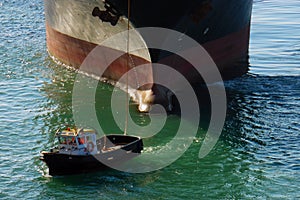 Big container ship in port with small boat in front. Huge cargo boat black and red follow mooring service boat. Vessel in habour