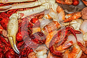 Big crab leg craw and mud bugs on top of pile of shrimp and onions and potatoes at seafood boil - selective focus photo