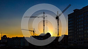 Big crane silhouette and many workers building new construction under a beautiful colorful sunset sky.Tall building under