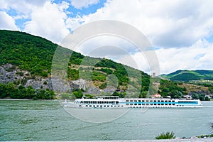 Big cruise ship on Danube river and mountains in background.