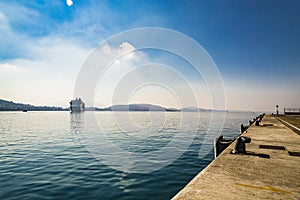 Big cruise ship sails to the sea port of Saranda, Albania. Albanian mountains at the background. Sunset, cloudy sky