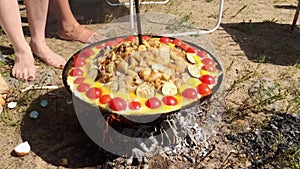 Big dish fool of potatoes and vegetables on a bonfire in summer sunny day.