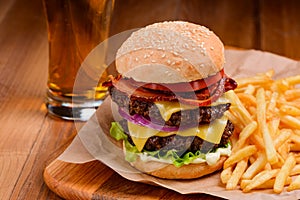 Big double cheeseburger served with handful of French fries and glass of beer
