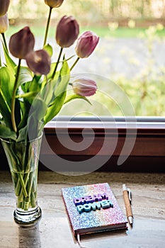 Big dream word on pop color rainbow unicorn shiny notepad and tulips on wooden table. Motivation quote, inspiration