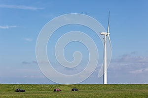 Dutch wind turbine near dike with parked cars photo