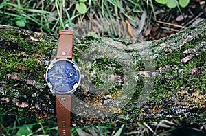 Big elegant men`s watch is lying on the tree with green moss outdoors. Stylish fashion accessories in the nature. Copys space