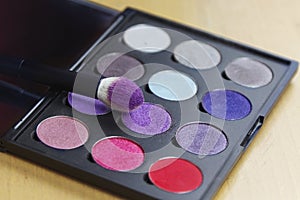 Big eye shadow palette of many colors shades in lilac, violet and red tones, with make up brush of bright lilac powder.