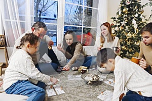 Big family gathering near Xmas tree playing lotto board game at home during Christmas holidays