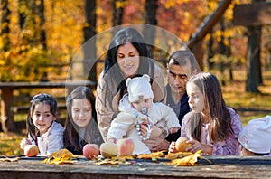 big family has picnic in autumn city park, children and parents sitting together at the table, with apples and yellow maple leaves