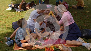 Big family having fun on picnic in city park. They interact with friend.