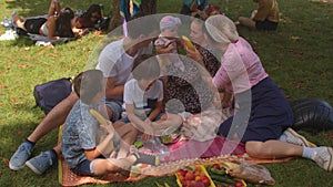 Big family having fun on picnic in city park. They interact with friend.