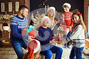 A big family in a room gives gifts at Christmas.