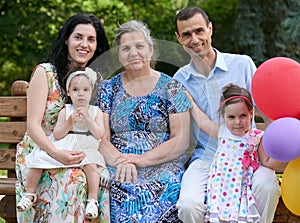 Big family sit on wooden bench in city park, summer season, child, parent and grandmother, small group of five people with balloon