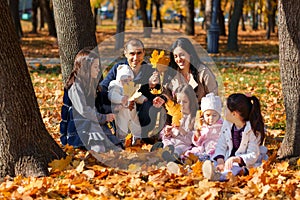 a big family sitting together in a glade of yellow maple leaves in an autumn city park, children and parents, happy people