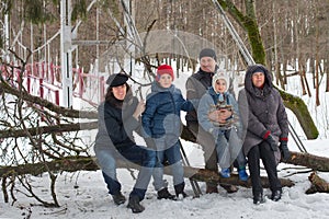 Big family are sitting on tree trunk in winter forest