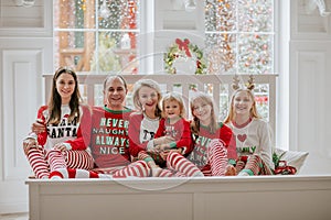 Big family of six in Christmas pyjamas sitting on white bed against big window with snow background