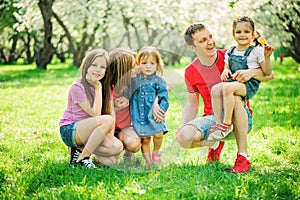 Big family with three little daughters spending time together in summer park, mother, father and sisters having fun